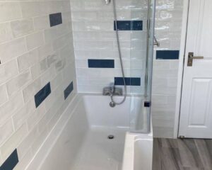 A new bathroom that has been fitted with white and blue wall tiles and a new shower over bath.