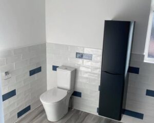 A new bathroom that has been installed with white and blue wall tiles, a new toilet and floating cabinet.