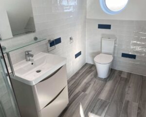 A new bathroom installation that has been fitted with new grey vinyl flooring, white tiled walls, a floating cabinet with integrated sink and a new toilet.