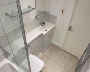 A new bathroom that has been installed with new cabinets and countertops, a new toilet, a shower enclosure, an integrated sink and floating glass shelves.