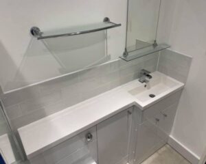 A new bathroom that has been installed with new cabinets and countertops, an integrated sink and floating glass shelves.