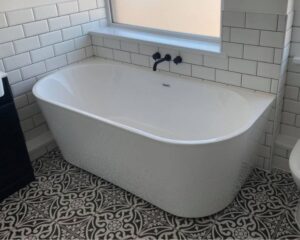 A bathroom that has been fitted with a new bathtub, along with white tiled walls and a mosaic-patterned tiled floor.