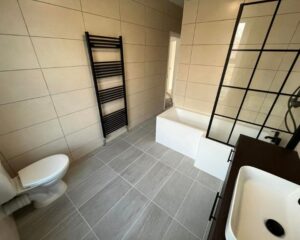 A new bathroom that has been fitted in a residential house in Southampton featuring grey floor tiles, beige wall tiles, a new shower over bath, cabinets with integrated sink and a new toilet.