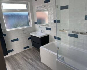A new bathroom that has been fitted with white and blue wall tiles and a new shower over bath, and a floating sink with integrated cabinet.