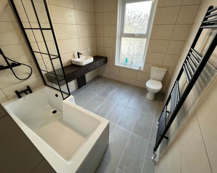 A new bathroom that has been fitted in a residential house in Southampton featuring grey floor tiles, beige wall tiles, a new shower over bath, cabinets with integrated sink and a new toilet.