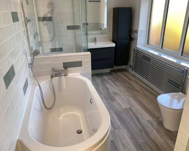 A new fitted bathroom in Southampton featuring laminate wooden flooring, a bathtub with integrated shower, blue bathroom cabinets with integrated sink and a new toilet.
