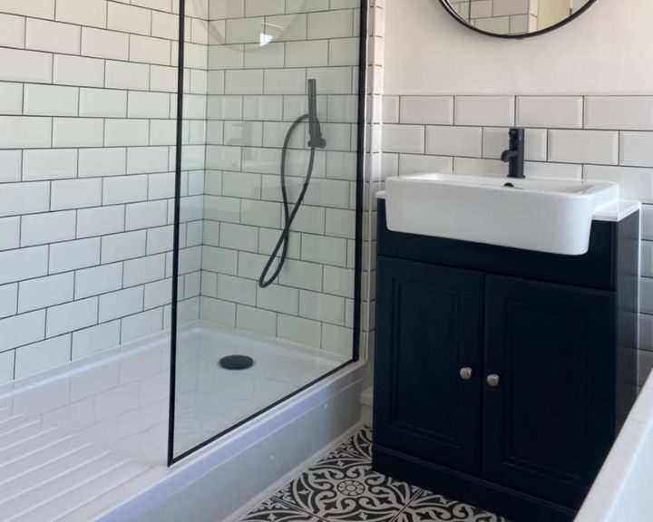 A bathroom that has been fitted with new white wall tiles, a new shower enclosure and a black cabinet with integrated sink.