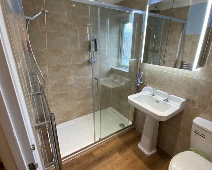 A new bathroom installation featuring wooden flooring, a shower enclosure, a new sink and toilet and marble-effect tiled walls.