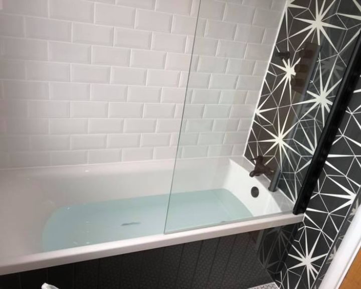 A bathroom installation that has been fitted with black and white patterned feature wall, white wall tiles and a new bath with shower screen.