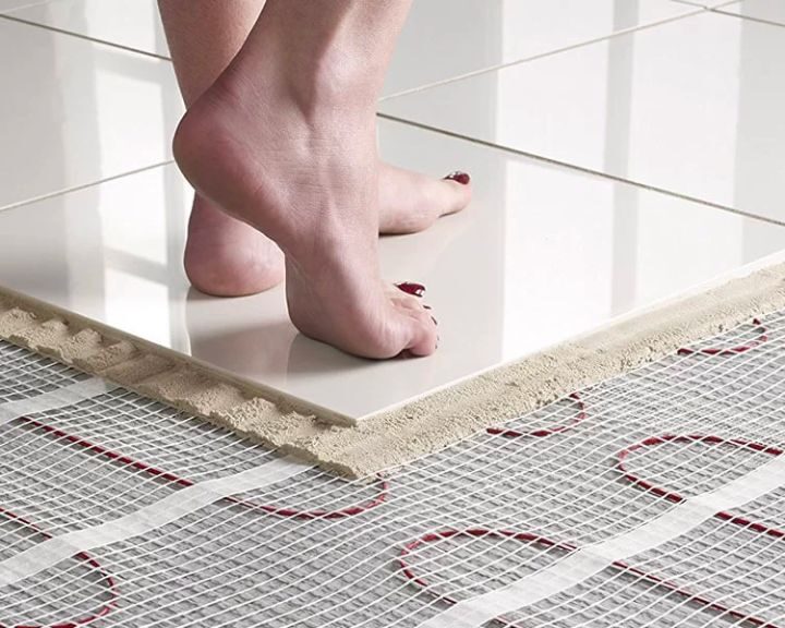 A woman's bare feet walking on a tiled bathroom floor with underfloor heating underneath.