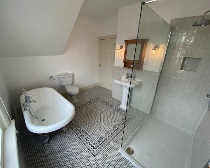 A wet room installation in Southampton featuring a walk-in shower, mosaic tiled floors, a free-standing bathtub, new toilet and sink.